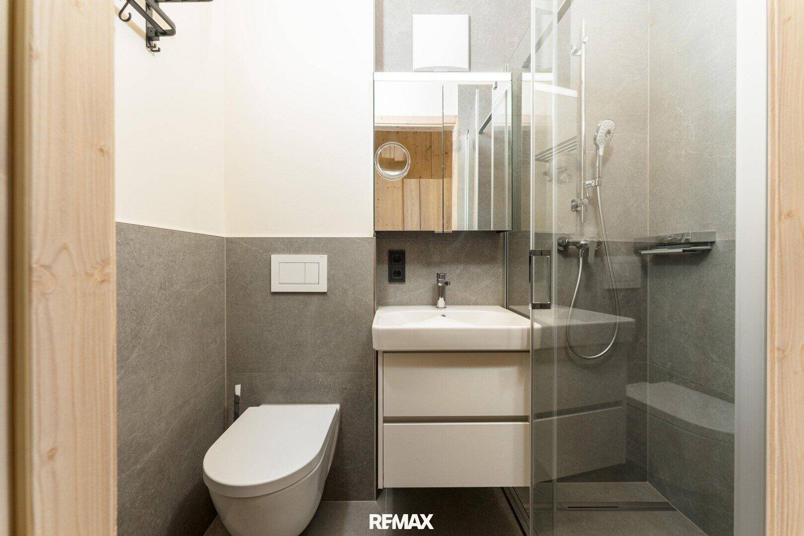 Modernes Badezimmer mit Dusche, wandhängendem WC und Spiegelschrank.