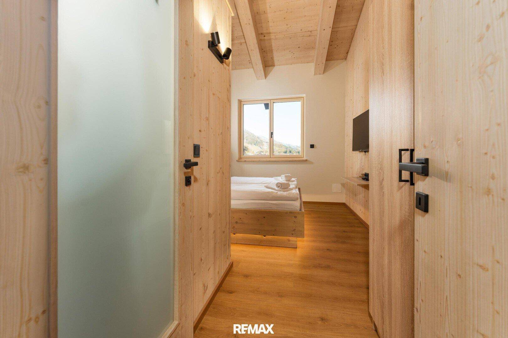 Heller Flur mit Holzverkleidung und Blick in ein Schlafzimmer mit Holzboden.