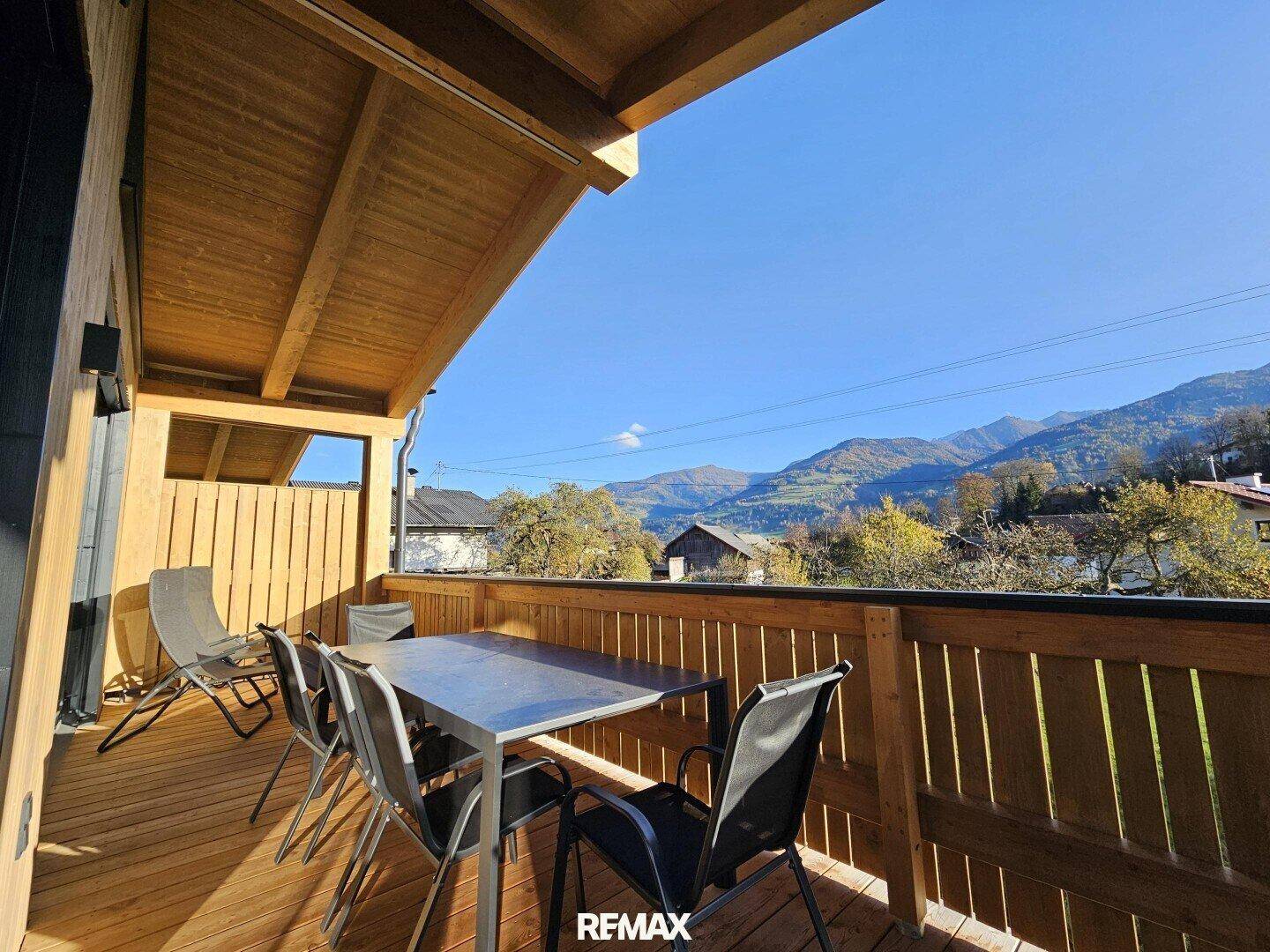 Heller Balkon mit Holzdielen und Sitzgruppe, bietet eine schöne Aussicht auf die umliegende Bergwelt.