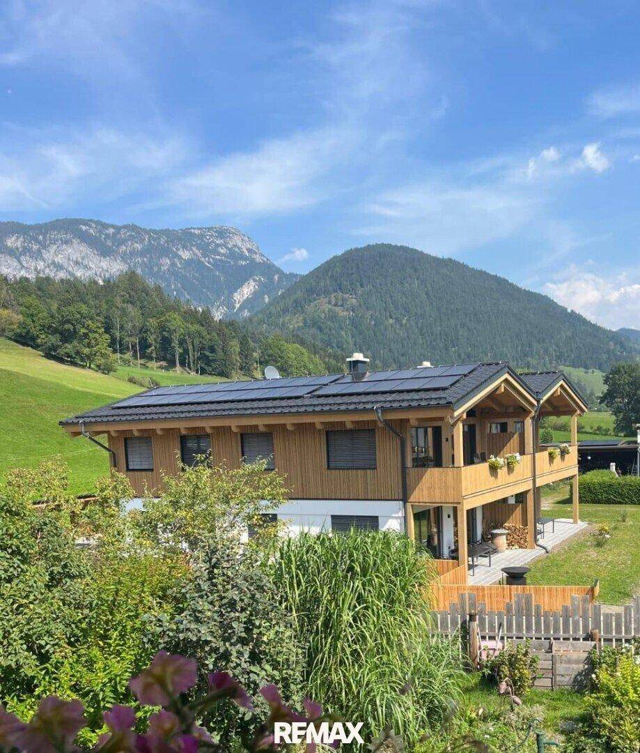 Modernes Chalet mit Solaranlage auf dem Dach, eingebettet in eine grüne Berglandschaft.