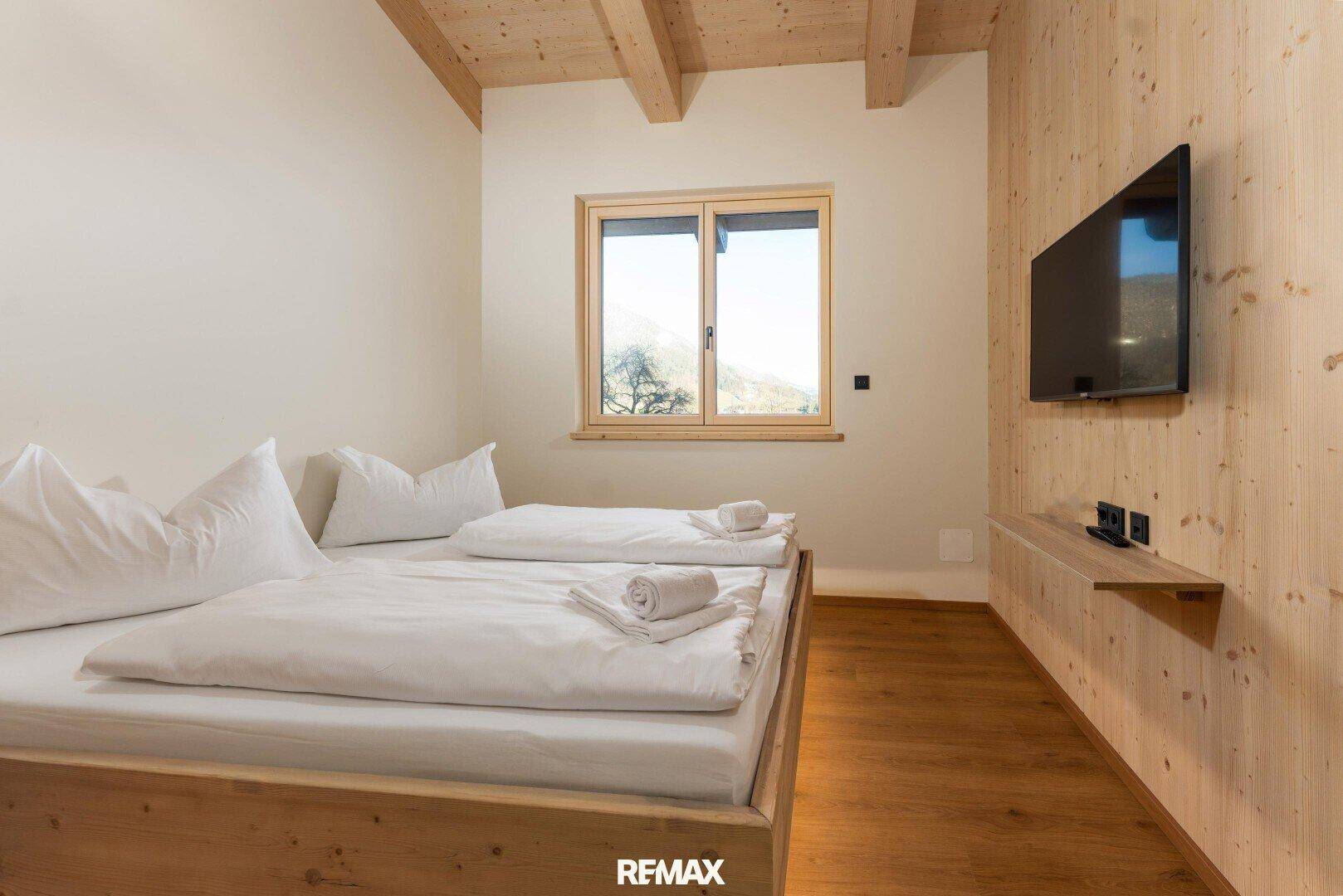 Gemütliches Schlafzimmer mit Holzbett, Holzboden und Fenster mit Blick auf die Natur.