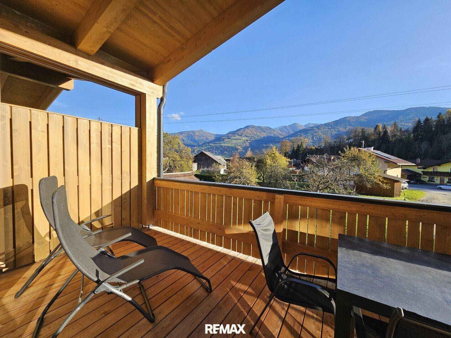 Sonniger Balkon mit Holzfußboden und Sitzgelegenheiten, bietet einen weiten Bergblick.