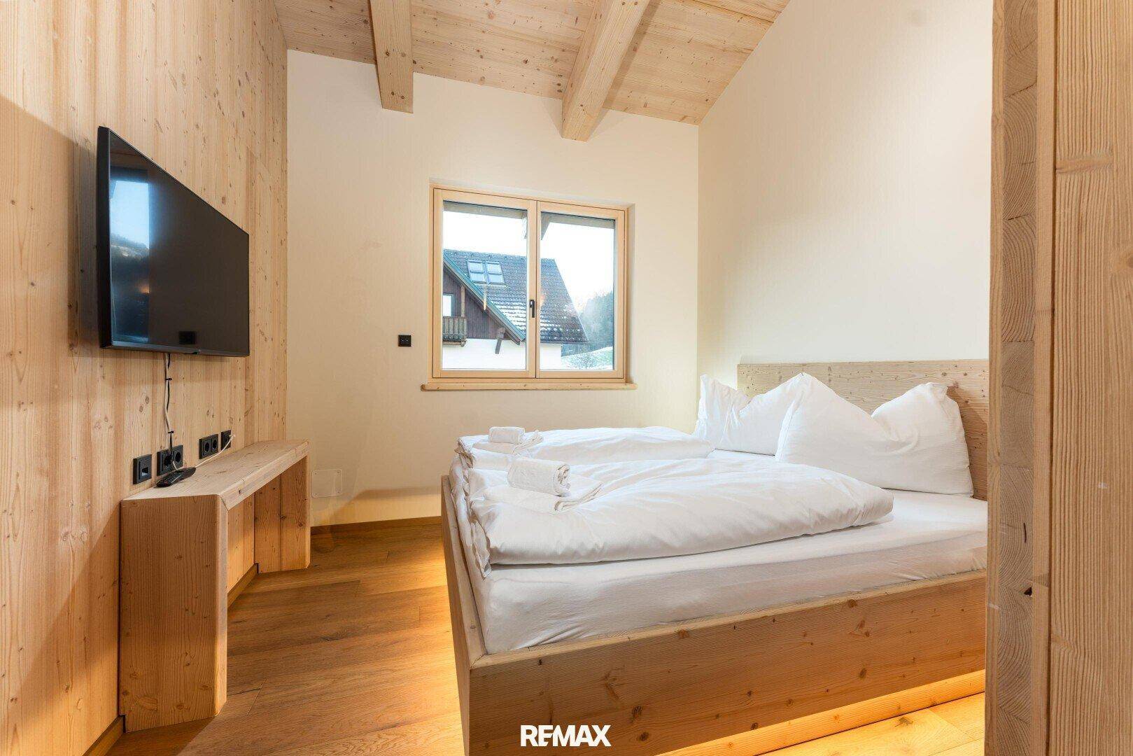 Gemütliches Schlafzimmer mit Holzbett, Holzboden und Fenster mit Blick auf die Umgebung.
