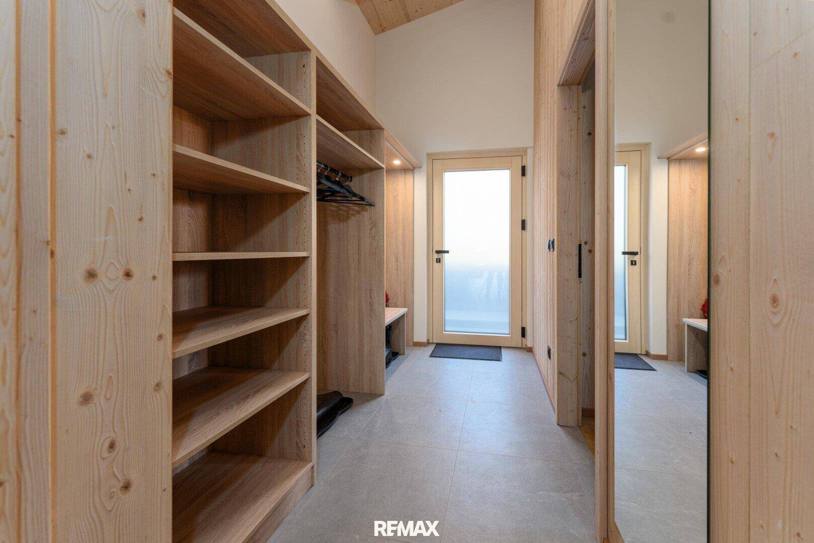 Geräumiger Eingangsbereich mit Holzregalen und Spiegel, ideal als Garderobe.