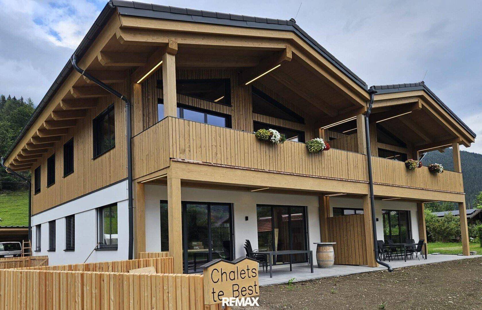 Modernes Chalet mit Holzfassade, Terrasse und Bergblick unter bewölktem Himmel.