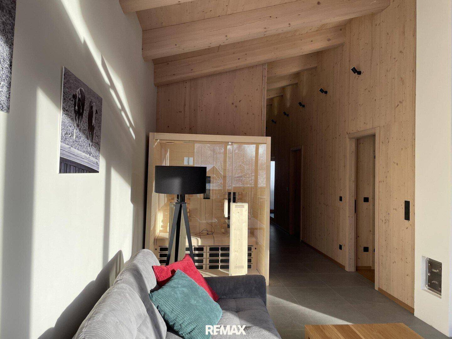 Wohnbereich mit bequemer Couch, Stehlampe und einer modernen Sauna mit Glasfront.