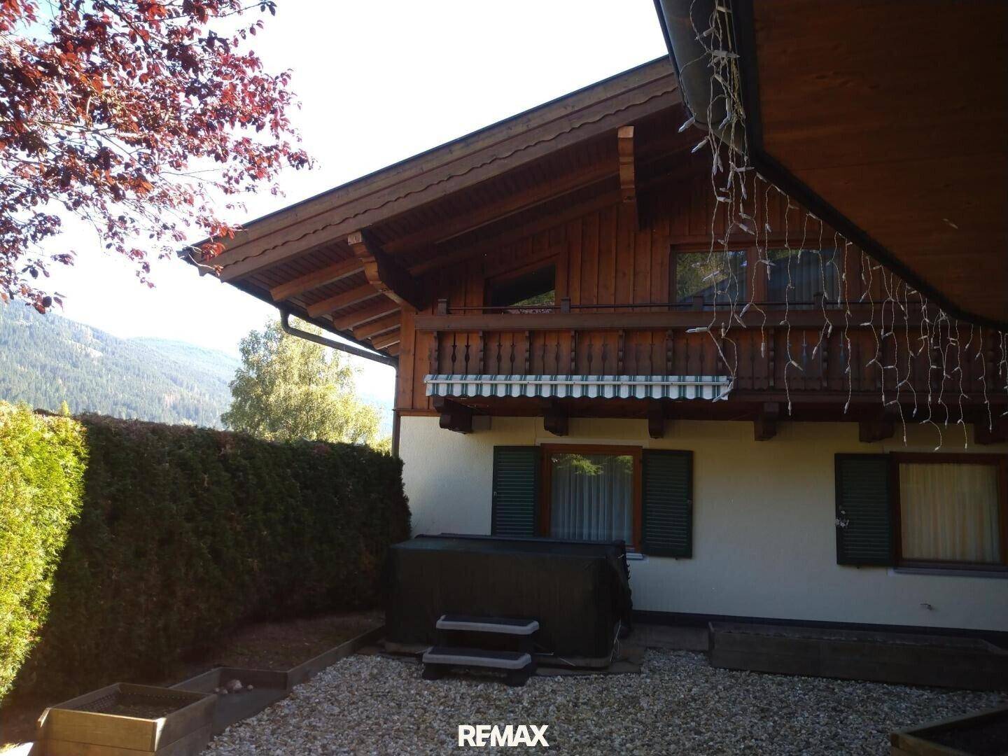 Kleiner Außenbereich mit Whirlpool und einem traditionellen Holzbalkon darüber, umgeben von Hecken und Bäumen.