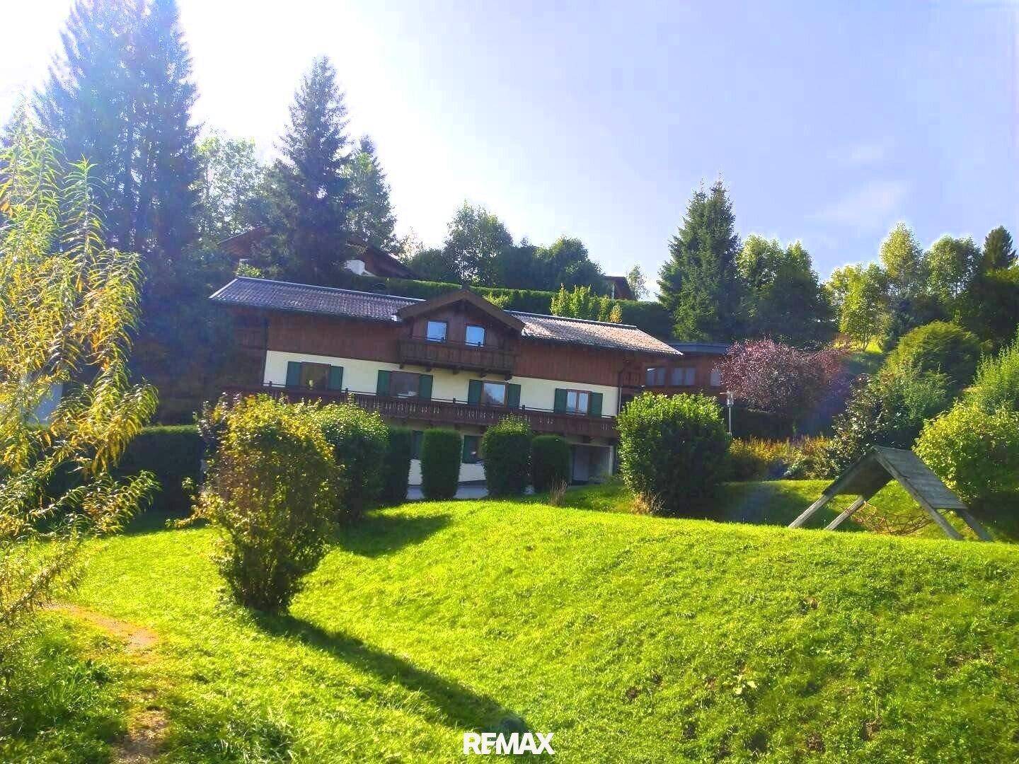 Großzügiger Gartenbereich mit Rasenflächen und Sträuchern vor einem traditionellen Haus in alpiner Umgebung.