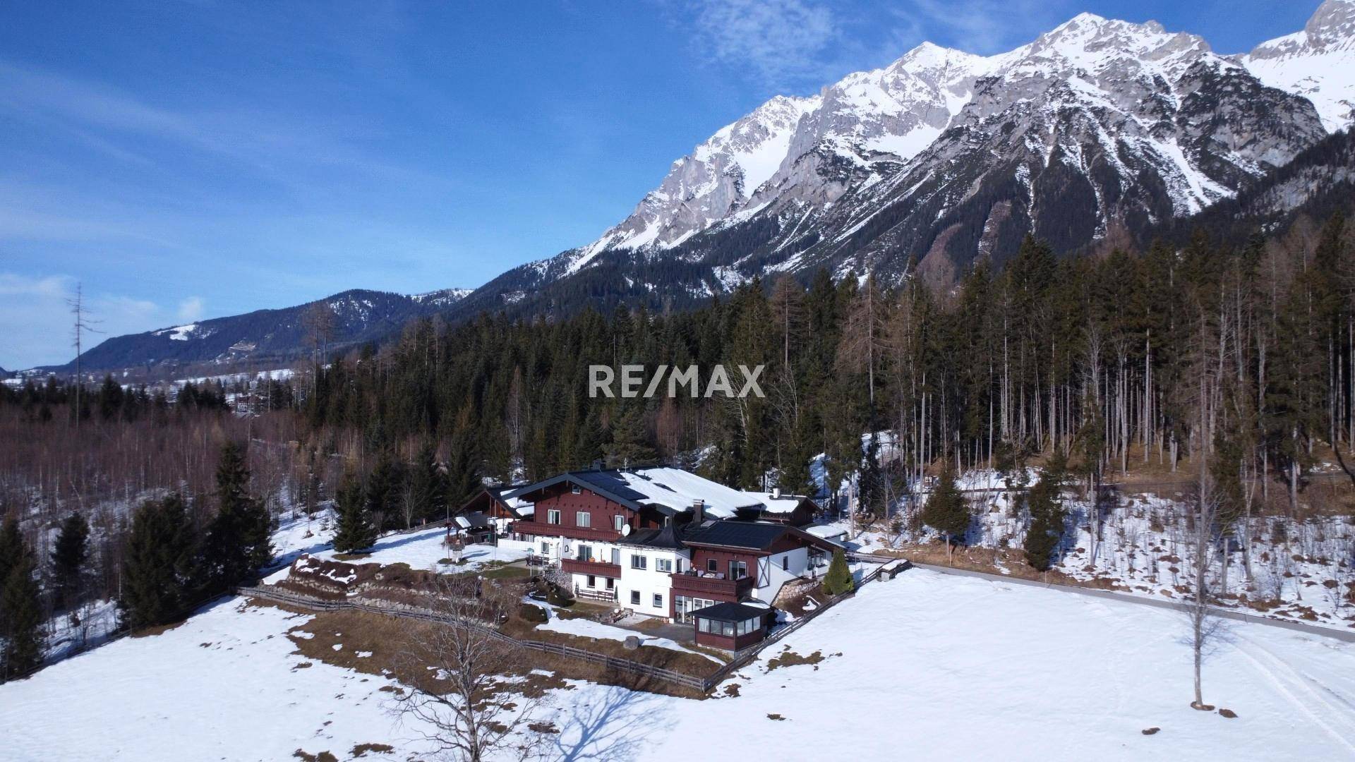 Luftaufnahme des weitläufigen Anwesens in alpiner Umgebung, umgeben von Wald und schneebedeckten Bergen.