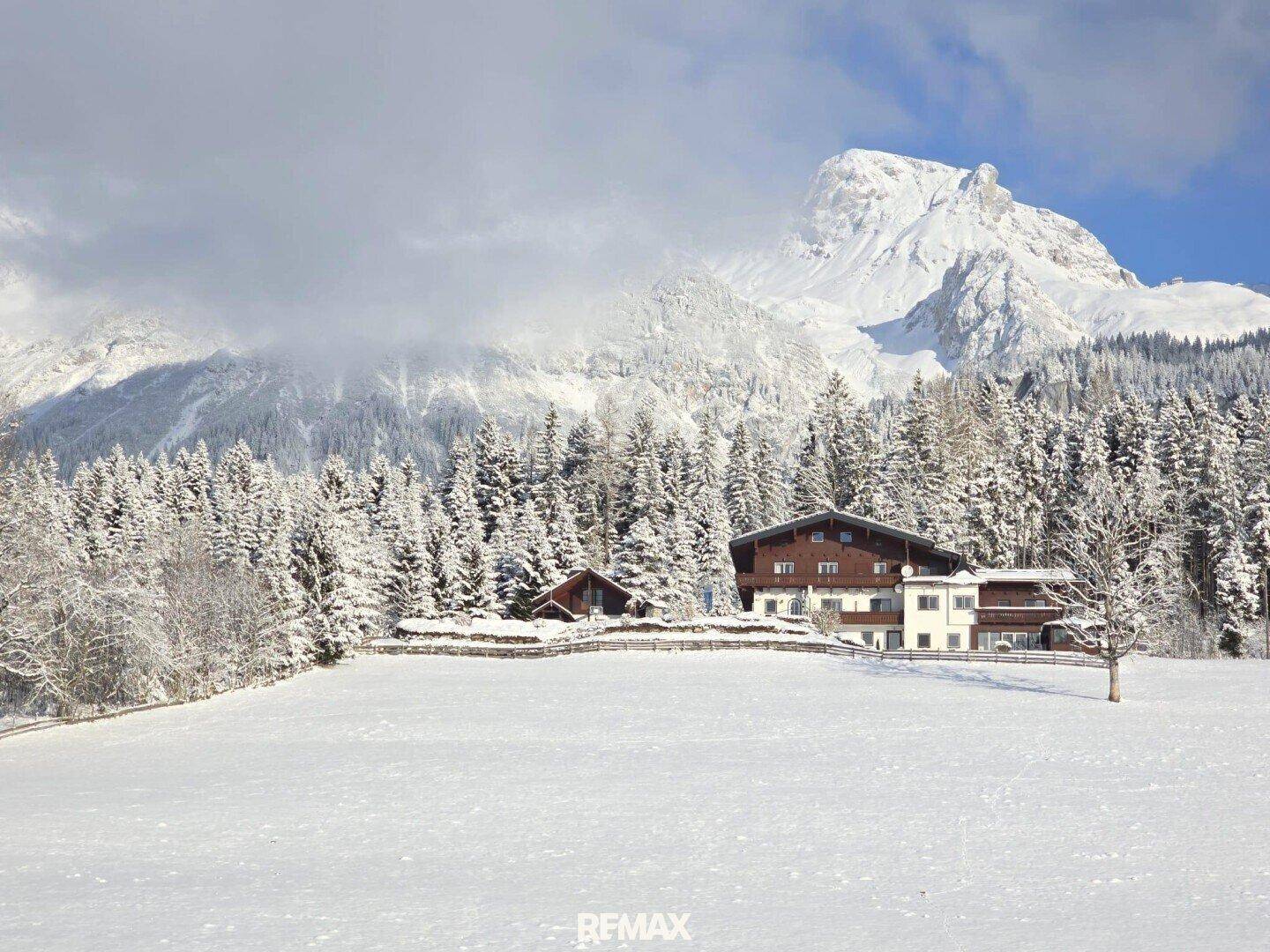 Charmantes Haus in einer tief verschneiten Winterlandschaft, umgeben von dichten Wäldern und Bergen.