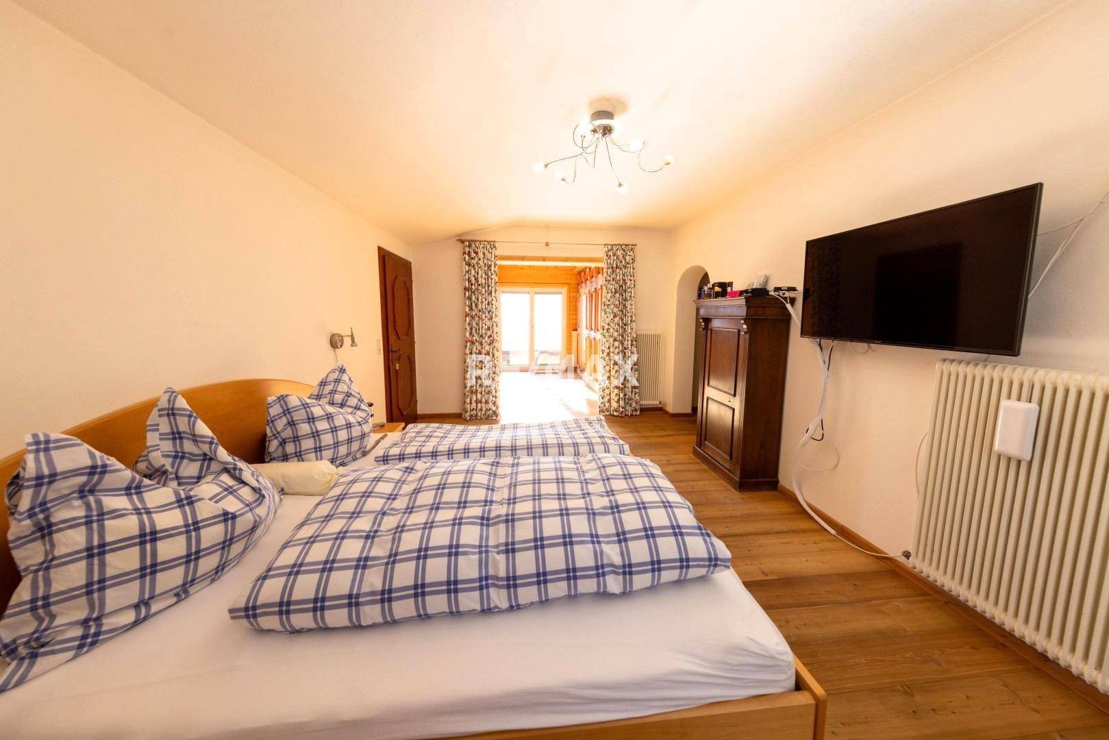 Helles Schlafzimmer mit zwei Einzelbetten, Holzboden und Zugang zu einem Balkon.