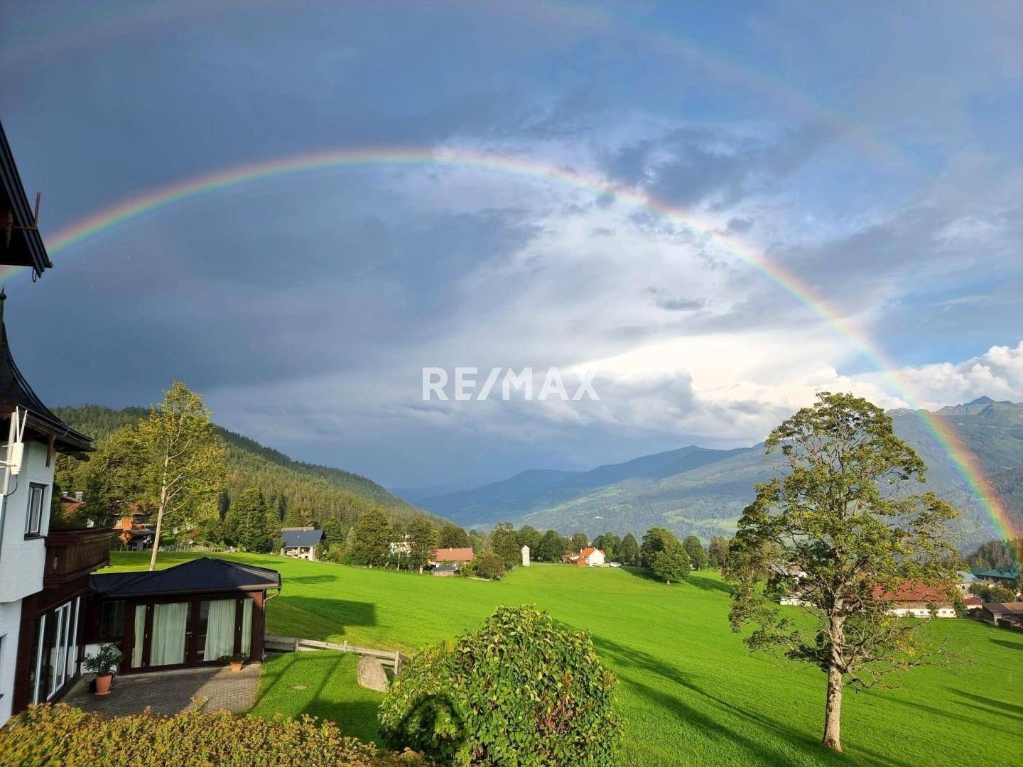 Malerische Landschaft mit Regenbogen über grünen Hügeln und einem Teil des Anwesens im Vordergrund.