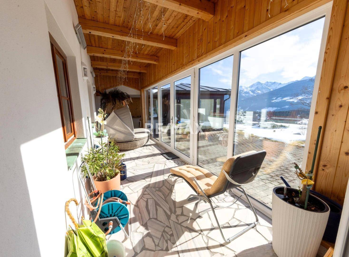 Heller Wintergarten mit großen Glasfronten, Holzbalkendecke und Panoramablick auf die Berge.