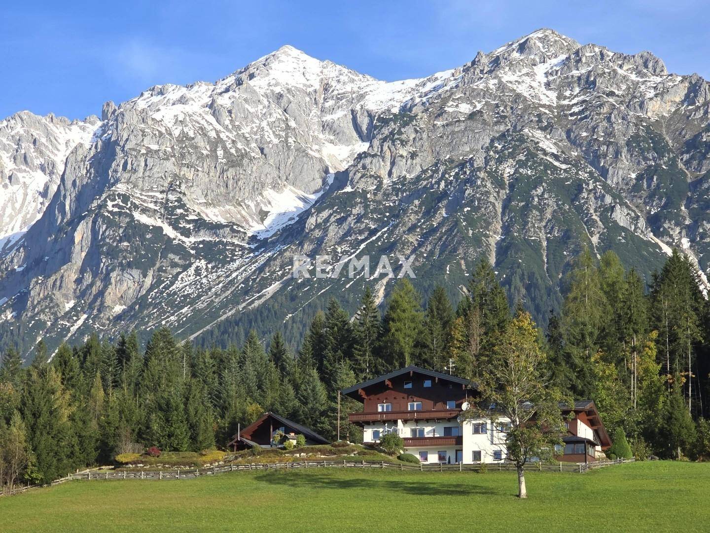 Großzügiges Anwesen in grüner Alpenlandschaft mit majestätischem Bergblick unter blauem Himmel.