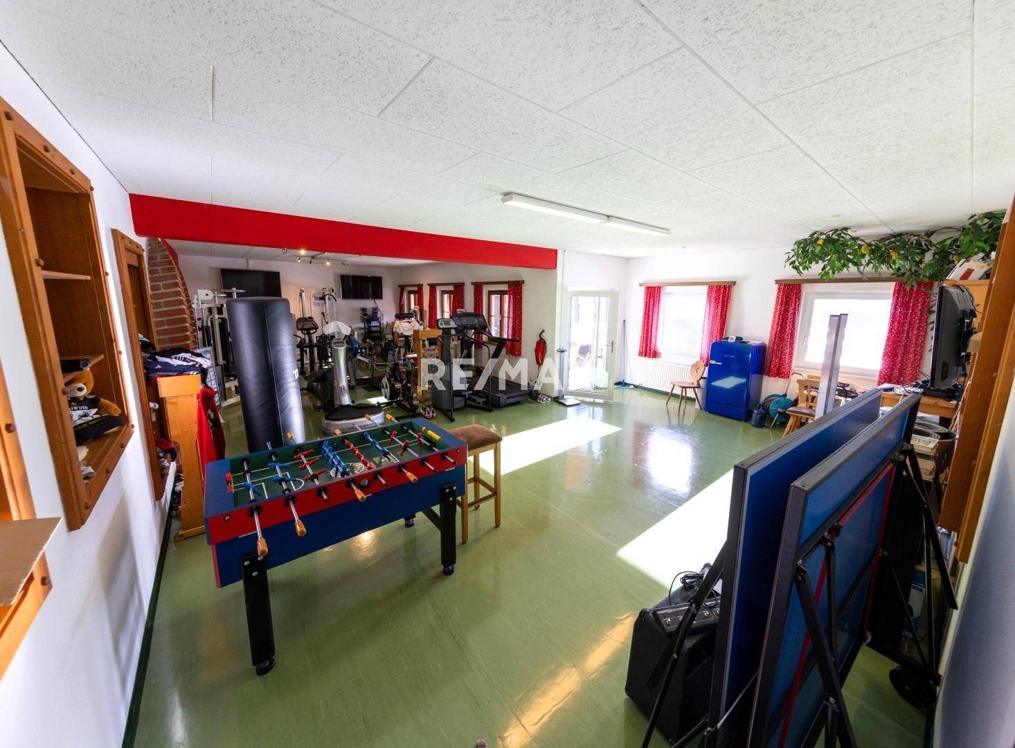 Großer Fitnessraum mit verschiedenen Trainingsgeräten, Tischfußball und Tischtennisplatte.