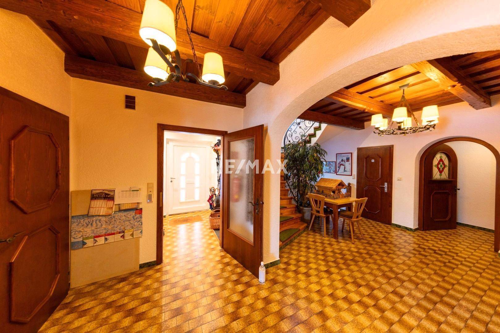 Geräumiger Eingangsbereich mit Holzbalkendecke, gefliestem Boden und geschwungener Treppe im Landhausstil.