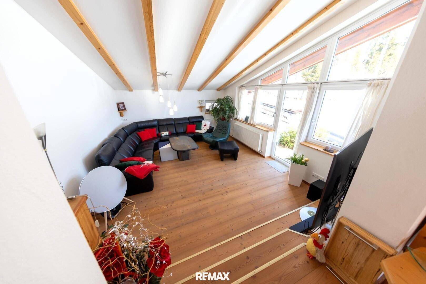Helles Wohnzimmer mit großen Fenstern, Holzboden und einem bequemen Ecksofa für entspannte Stunden.