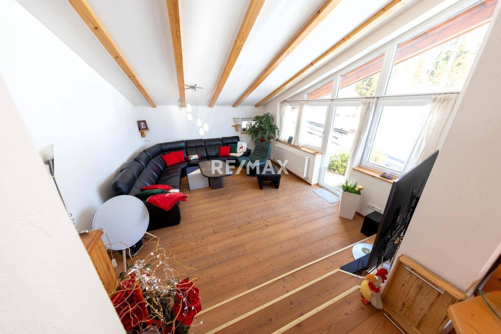 Helles Wohnzimmer mit Holzboden, hohen Fenstern und bequemer Sitzecke, ideal zum Entspannen.