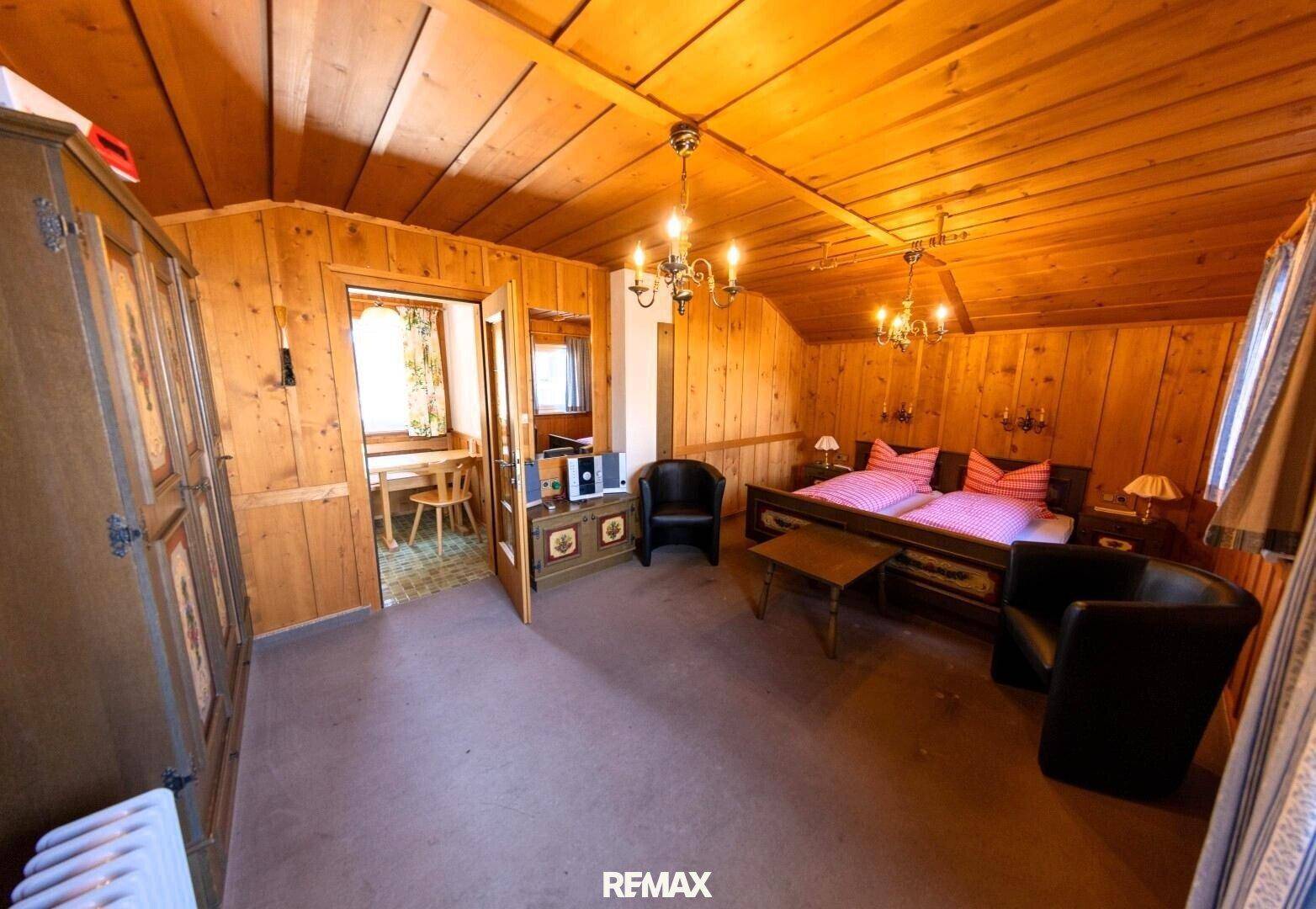 Traditionelles Schlafzimmer mit Holzvertäfelung, rustikalen Möbeln und einem kleinen Essbereich angrenzend.