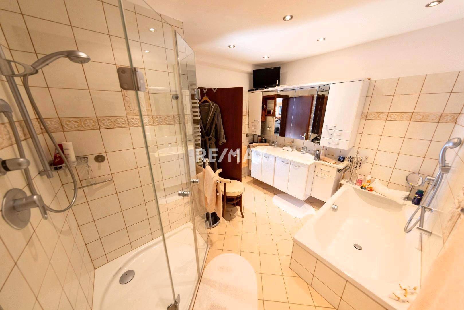 Geräumiges Badezimmer mit Dusche, Eckbadewanne, Doppelwaschbecken und hellen Fliesen.