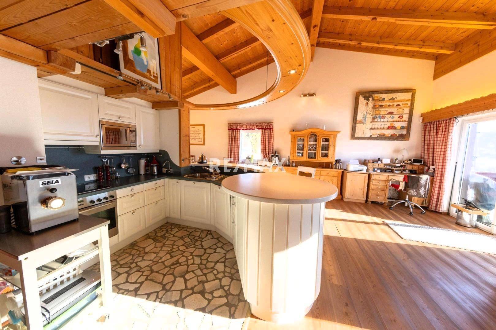 Offene Küche mit weißen Schränken, Steinboden und Holzbalkendecke, kombiniert mit Arbeitsbereich.