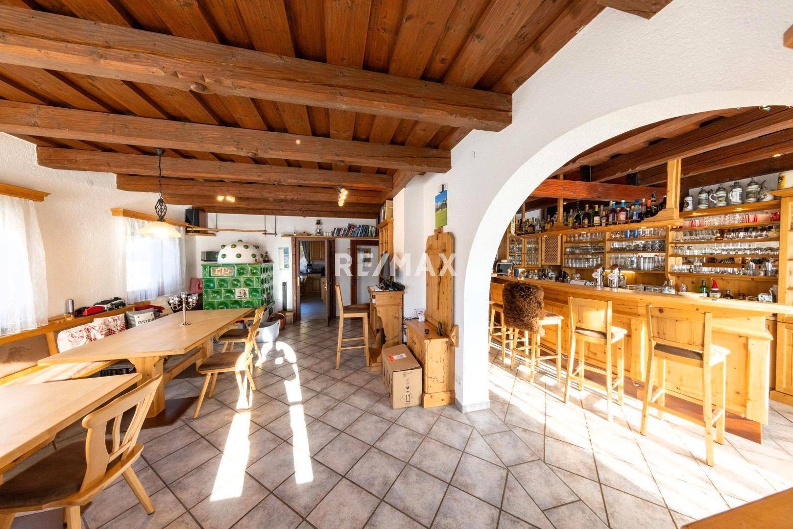 Rustikaler Wohn- und Essbereich mit Holzbalkendecke, Kachelofen und einer einladenden Bar.