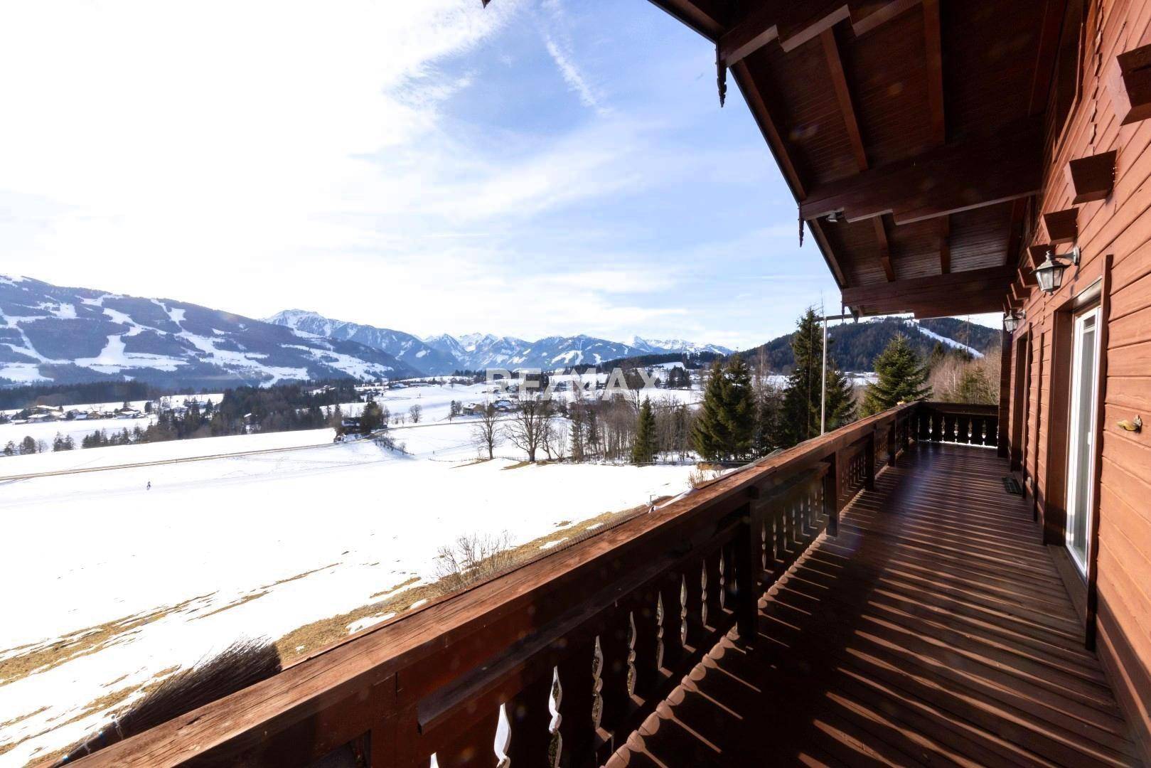 Langer Holzbalkon mit traditionellem Geländer und weitem Blick auf die verschneite Berglandschaft.