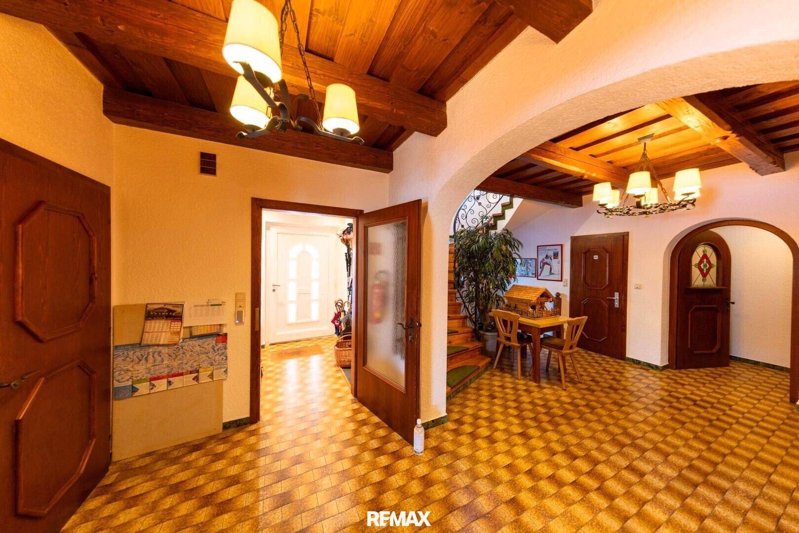 Geräumiger Eingangsbereich mit rustikalen Holzbalken, gemustertem Fliesenboden und einer geschwungenen Treppe.