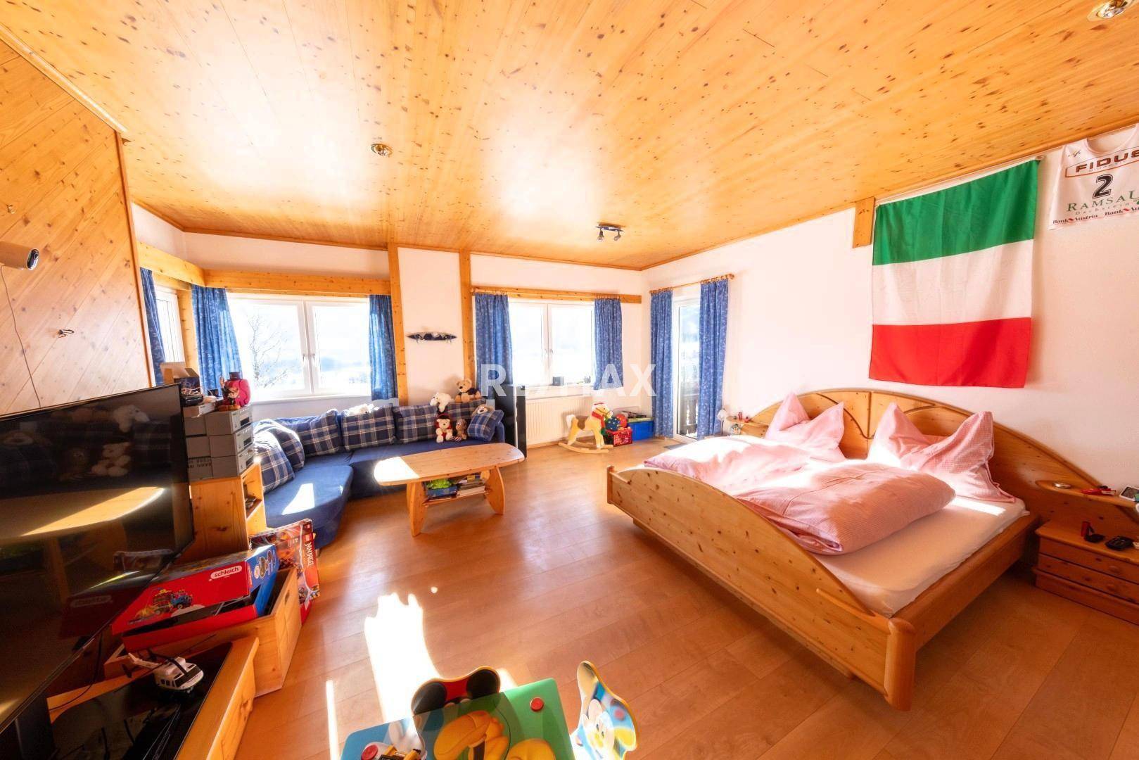 Helles Schlafzimmer mit Holzbett, Holzbalkendecke und großzügigen Fenstern mit Blick ins Grüne.