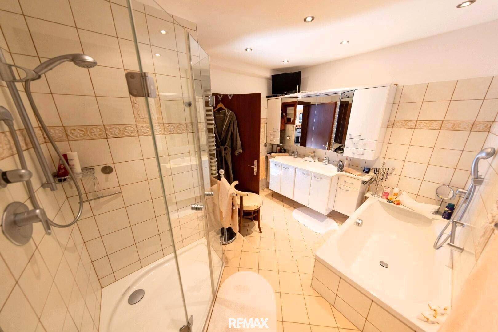 Modernes Badezimmer mit Duschkabine, Eckbadewanne, Doppelwaschbecken und hellen Fliesen.