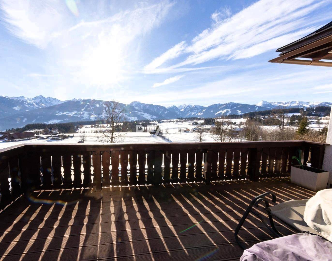 Breiter Holzbalkon mit weitem Blick über die verschneite Landschaft und die umliegenden Berge.