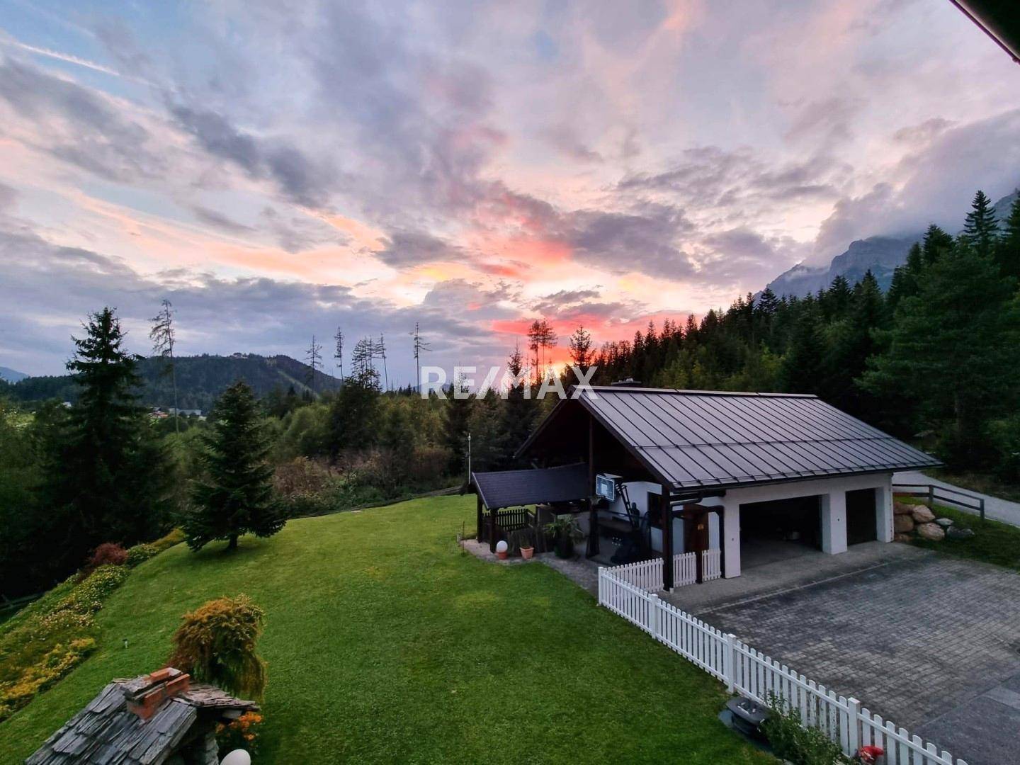 Abendliche Ansicht des Anwesens mit Carport und Garage, umgeben von grünen Hügeln und Wald.