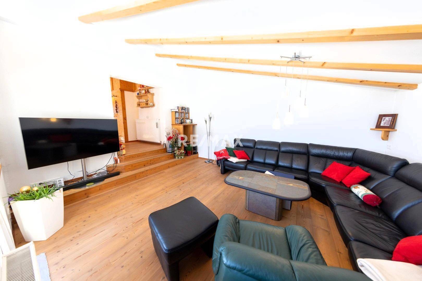 Gemütliches Wohnzimmer mit Holzboden, freiliegenden Holzbalken und großer schwarzer Ledercouch.