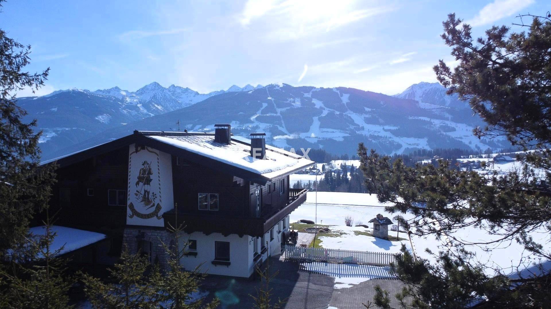 Traditionelles Alpenhaus mit Holzbalkonen und weitem Blick auf die verschneite Bergwelt und Skipisten.