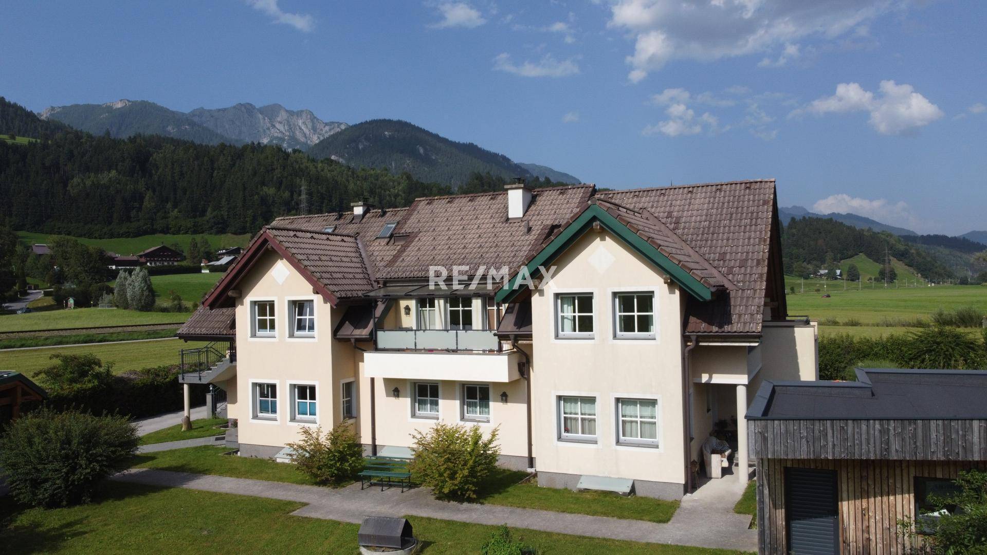 Charmantes Haus mit Balkon und gepflegtem Vorgarten vor einer beeindruckenden Bergkulisse.