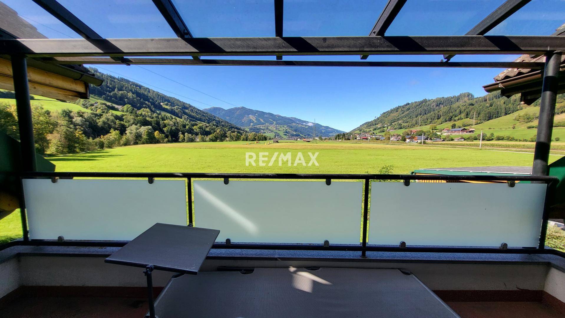 Überdachte Loggia mit weitem Blick über grüne Felder und die umliegende Berglandschaft.