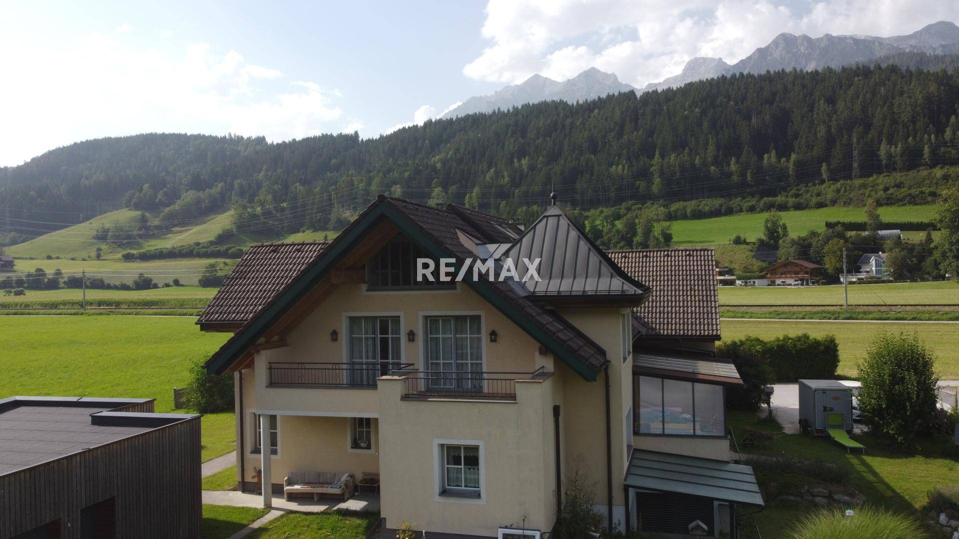 Ansicht des Hauses von oben mit markantem Dach und Balkonen vor einer Bergkulisse.