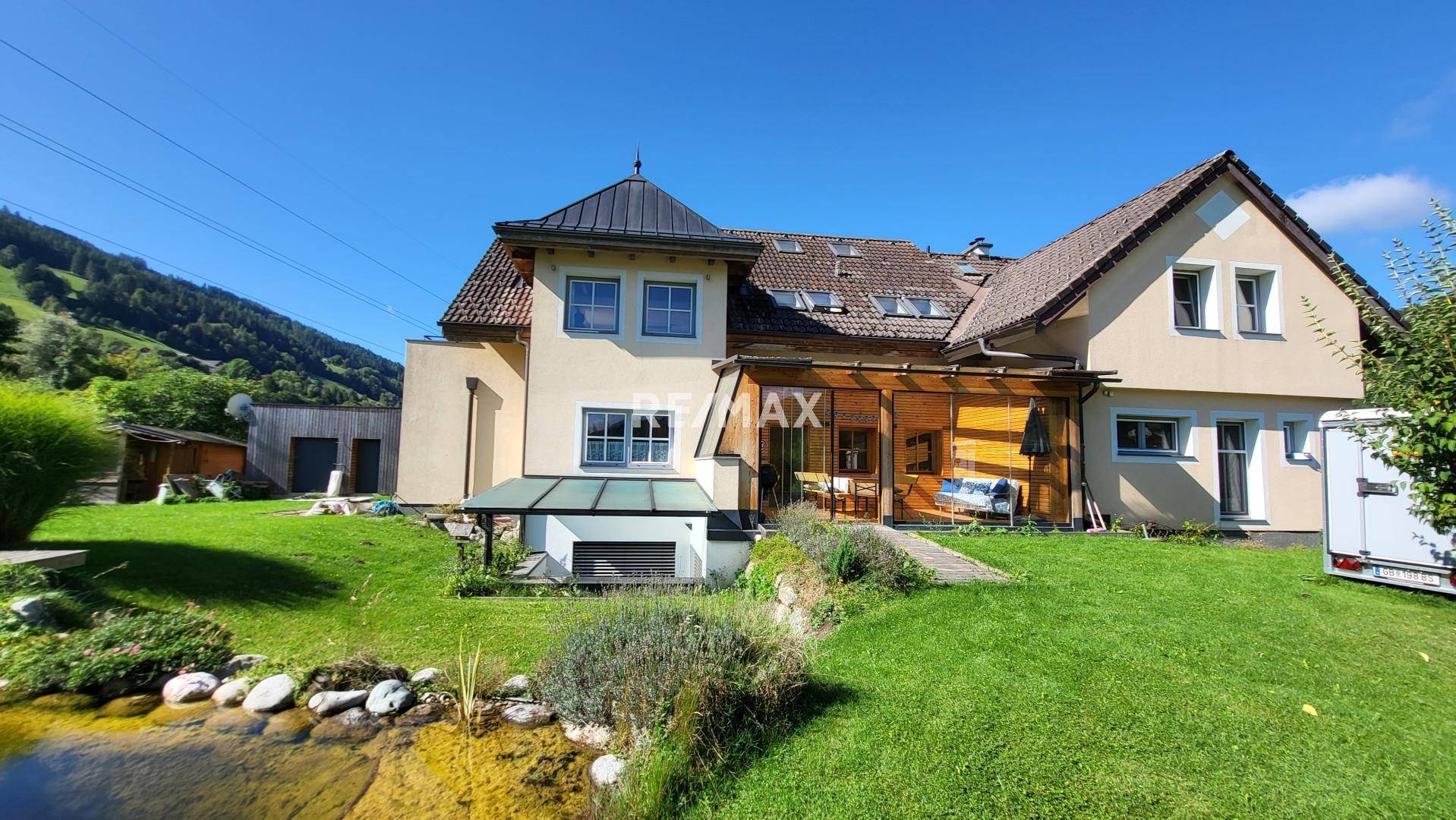 Rückseite des Hauses mit Teich, Garten und überdachtem Sitzbereich in ländlicher Umgebung.