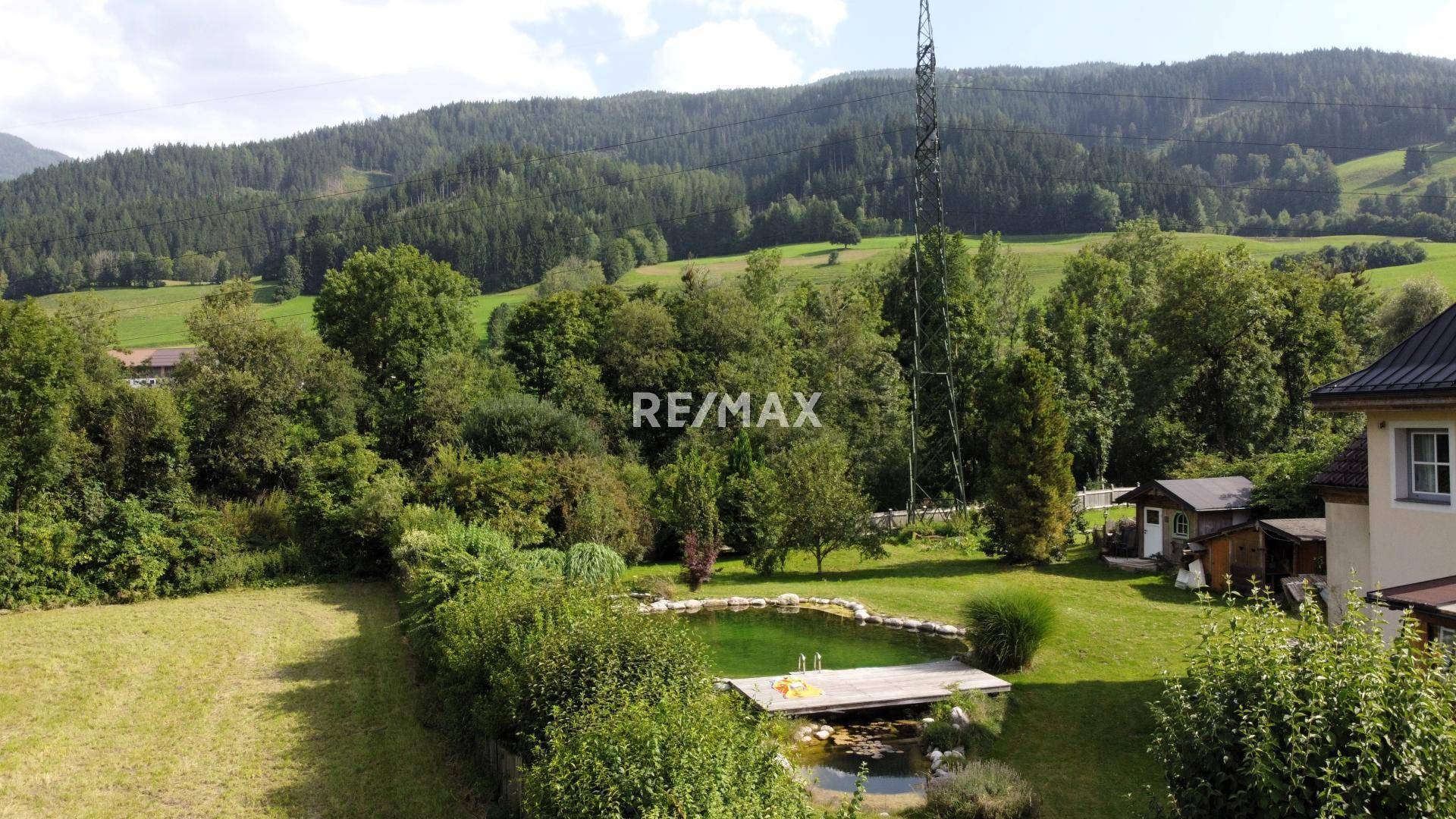 Weitläufiger Gartenbereich mit großem Teich und Holzsteg, umgeben von üppiger Natur.