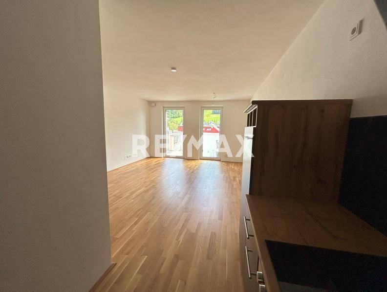 Blick vom Küchenbereich in den hellen Wohnraum mit Holzboden und Zugang zum Außenbereich.