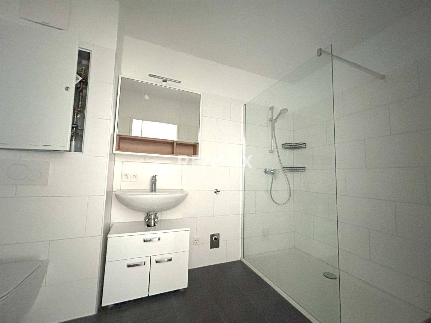 Modernes Badezimmer mit Duschkabine, Waschbecken und Wand-WC in hellen Fliesen.