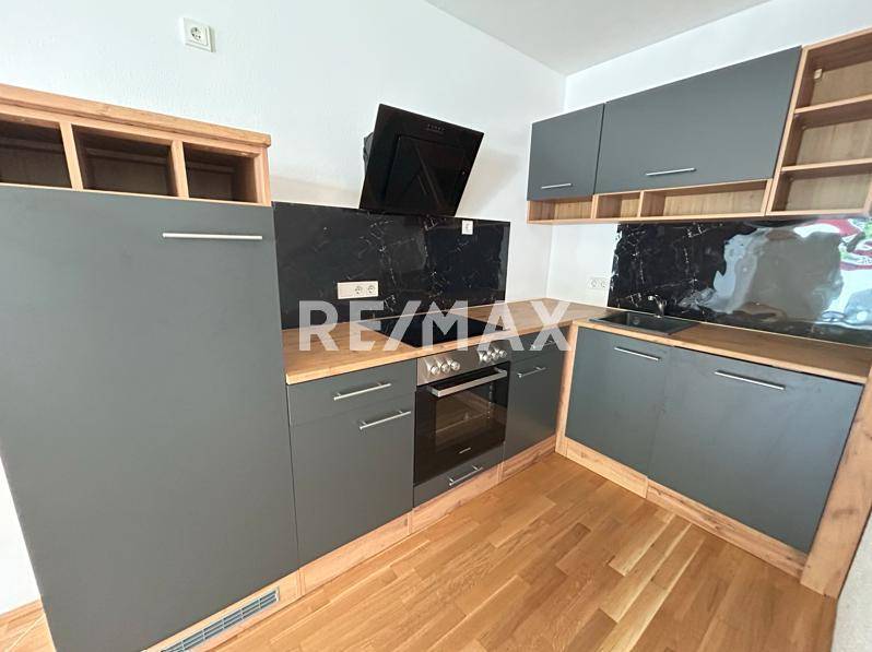 Moderne Einbauküche mit grauen Fronten, Holz-Arbeitsplatten und schwarzer Rückwand.