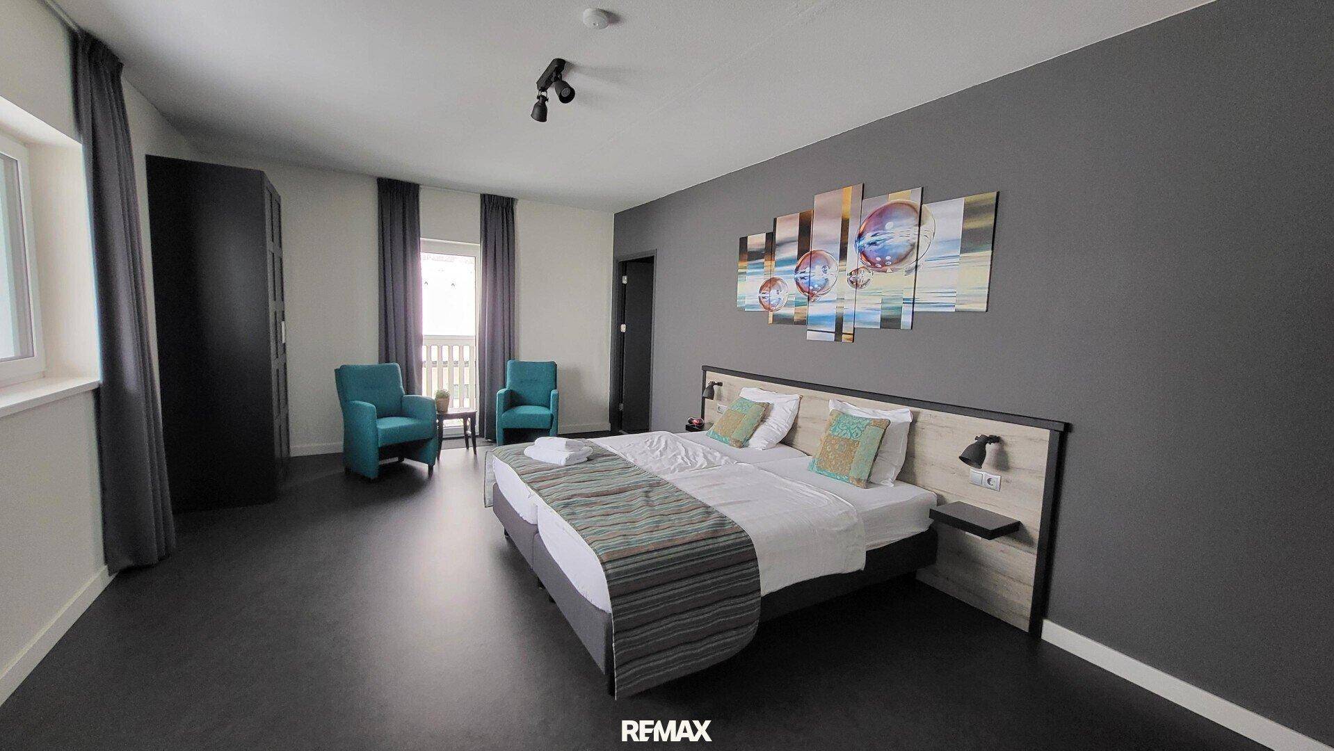 Modernes Schlafzimmer mit Doppelbett, farbigen Sesseln und Zugang zu einem Balkon.