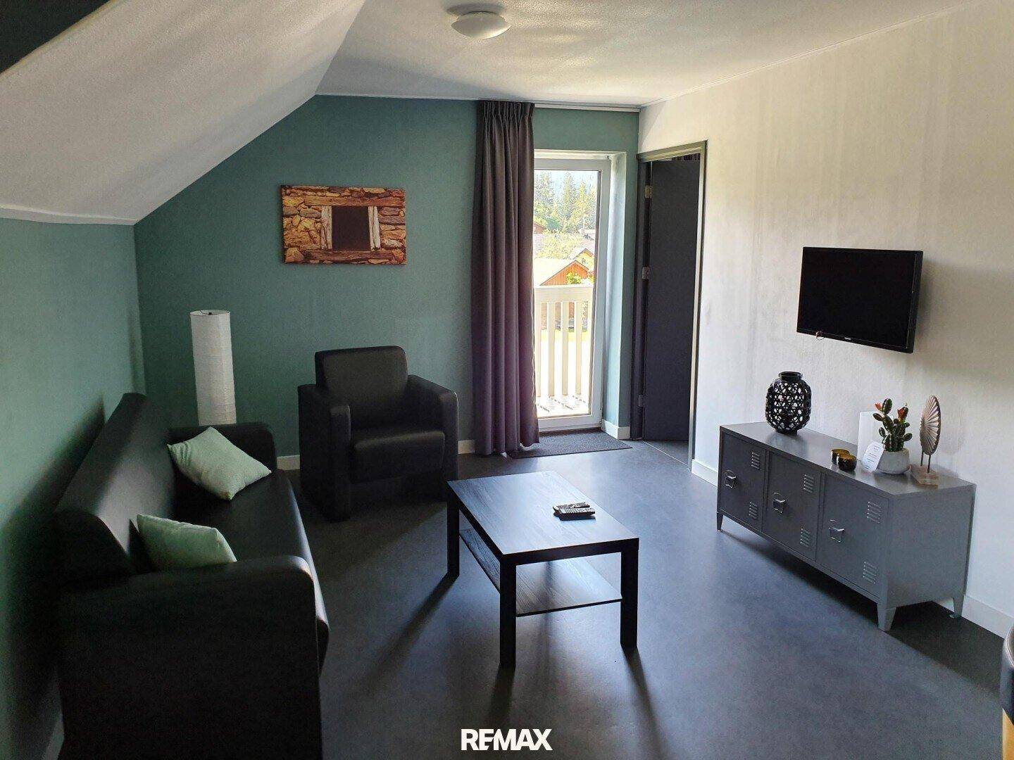 Gemütliches Wohnzimmer mit Sofa, Sessel, Couchtisch und Zugang zum Balkon.