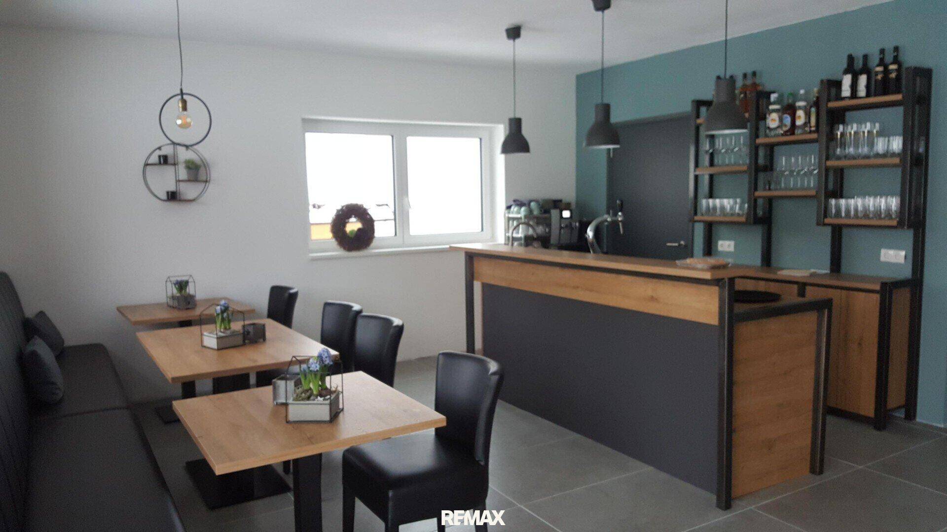 Moderner Gastraum mit Bar, Holztischen und bequemen Sitzbänken, ideal für gesellige Runden.