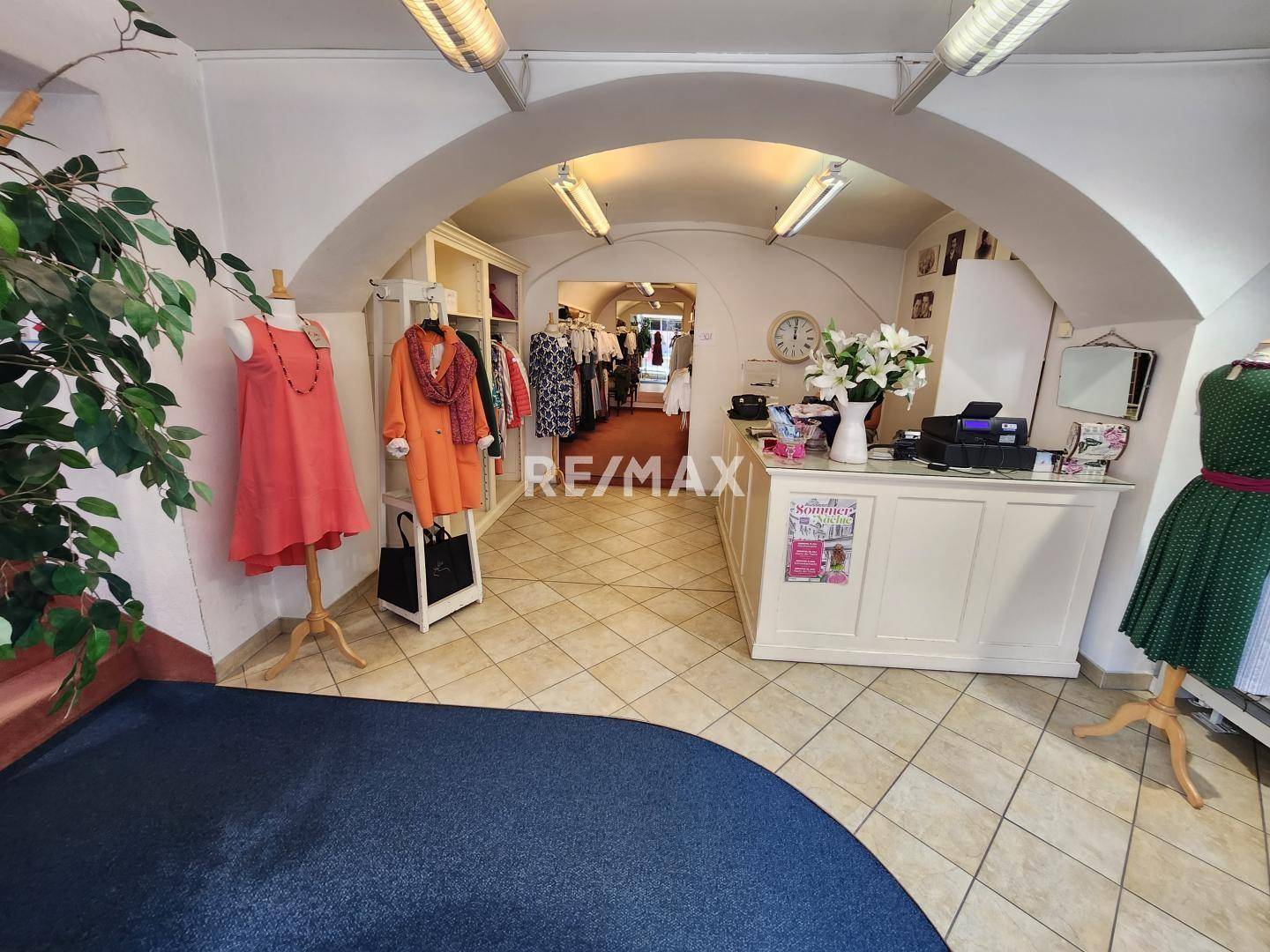 Heller Ladenbereich mit Gewölbedecke, Fliesenboden und Verkaufstheke, präsentiert Kleidung und Accessoires.