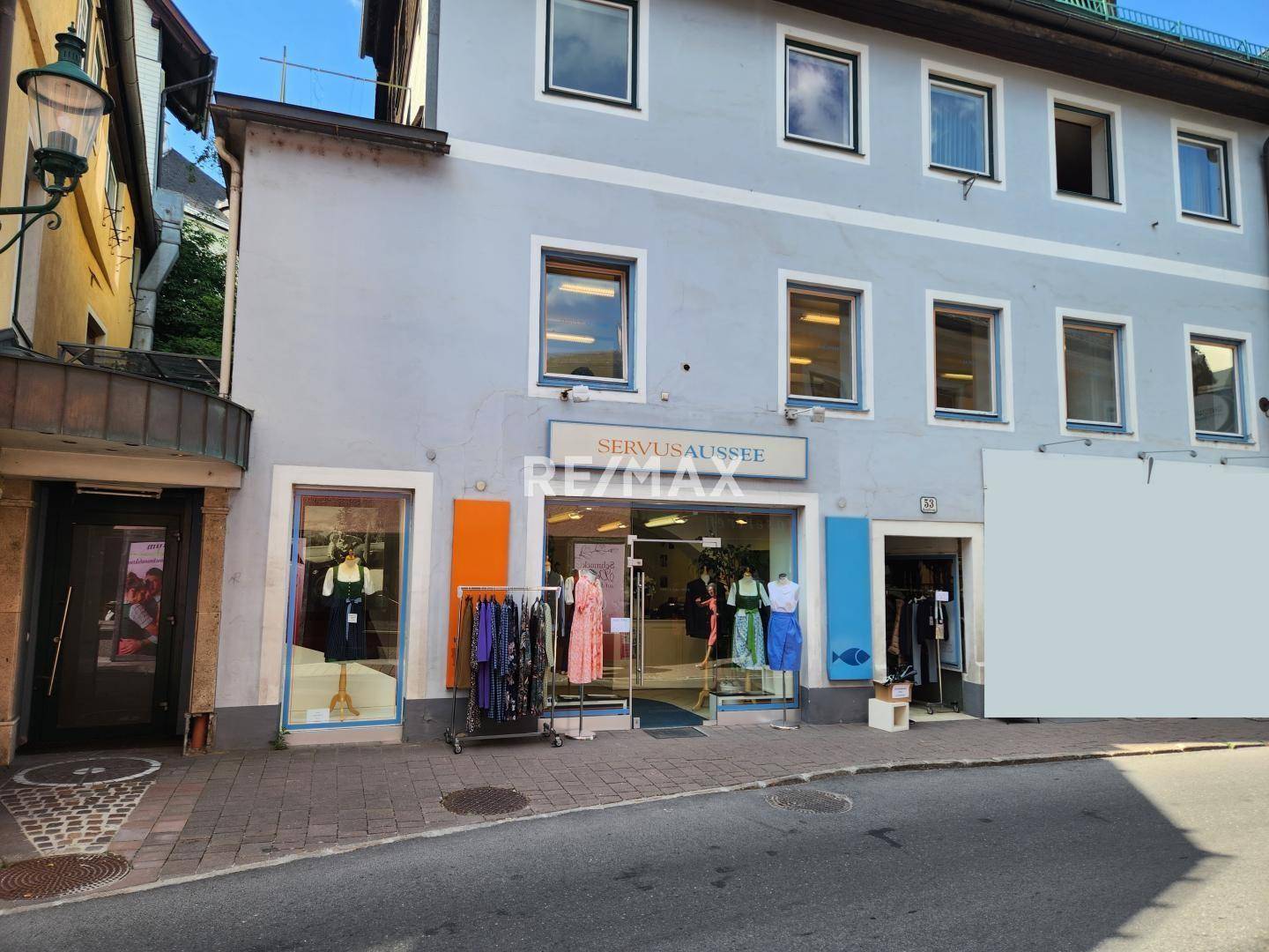 Geschäftsfassade mit großen Schaufenstern und Eingangsbereich, an einer belebten Straße gelegen, mit Auslagen.