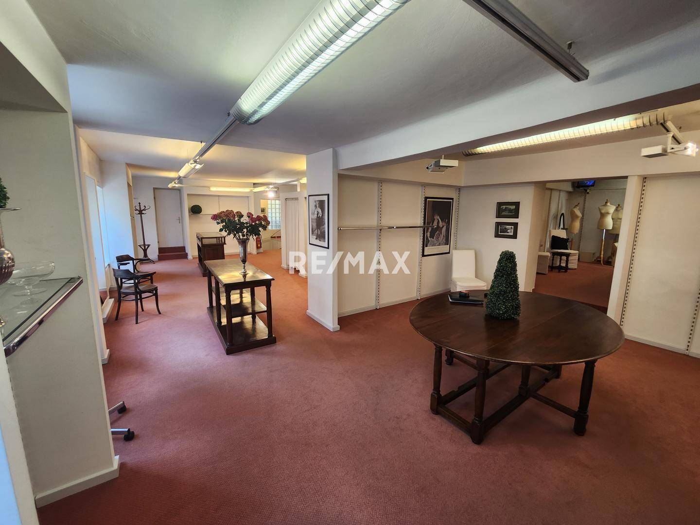 Großer Verkaufsraum mit rotem Teppichboden, verschiedenen Tischen und Regalsystemen, gut beleuchtet und einladend.