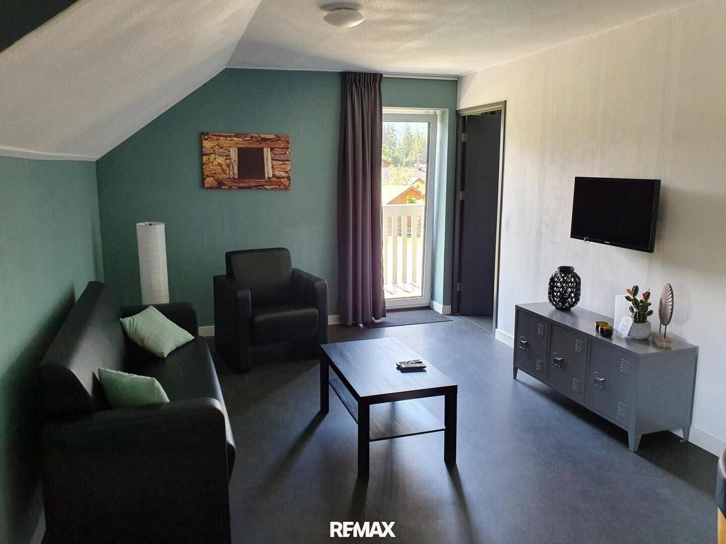 Wohnzimmer mit Sofa, Couchtisch und Fernseher, mit Zugang zu einem Balkon.