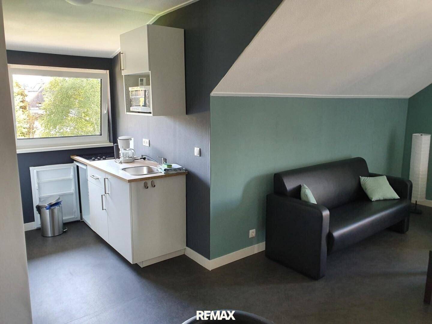 Kombinierter Wohn- und Küchenbereich mit kleiner Küchenzeile und Sofa unter Dachschräge.